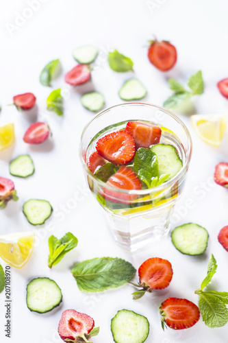 A glass of water with the addition of strawberries, cucumber, mint and lemon. In a circle of bright ingredients on a white background. Detox and Sports Concept
