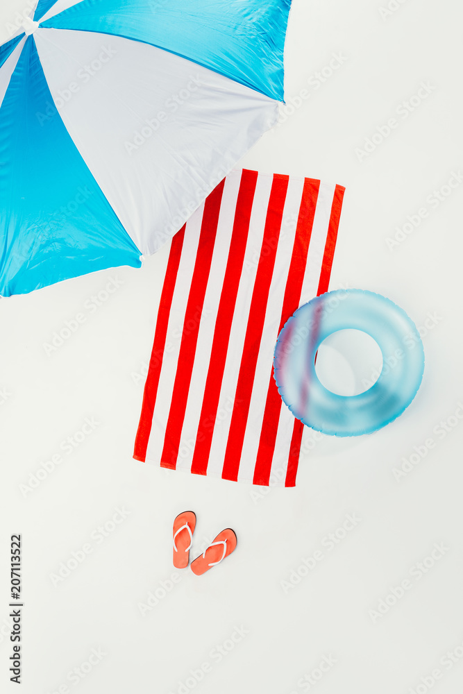 top view of beach umbrella, striped beach towel, flip flops and inflatable ring isolated on white top view of beach umbrella, striped beach towel, flip flops and inflatable ring isolated on white