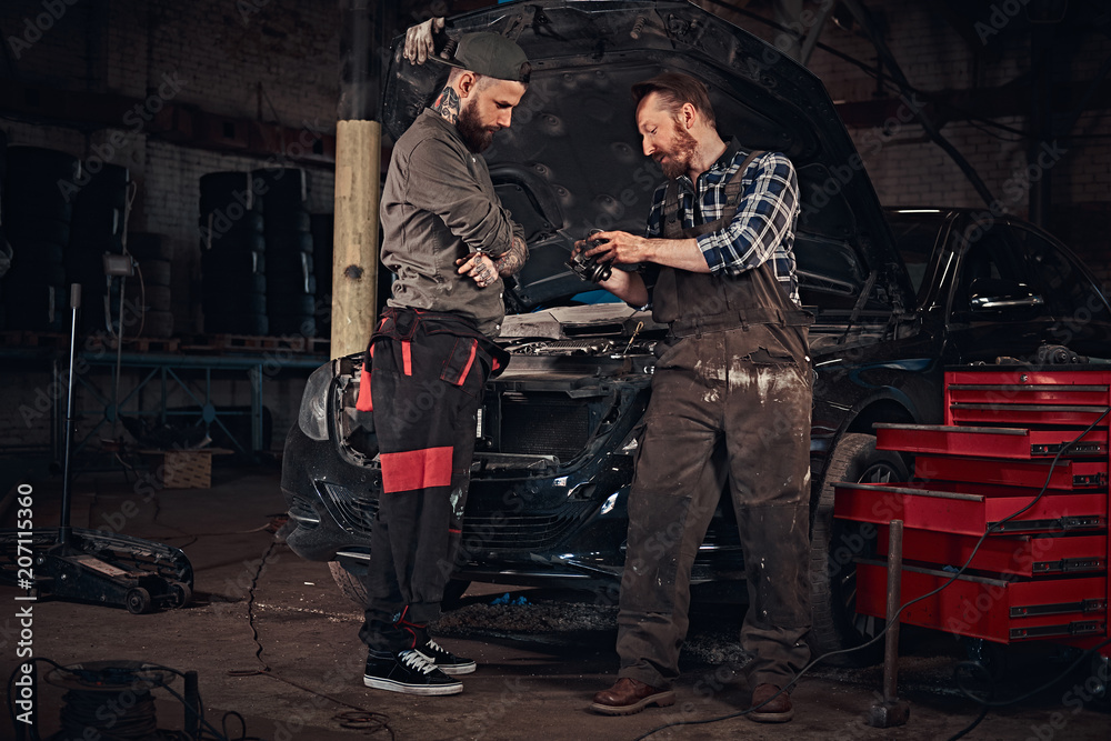 Two mechanic talking during repairs a broken car in a garage.