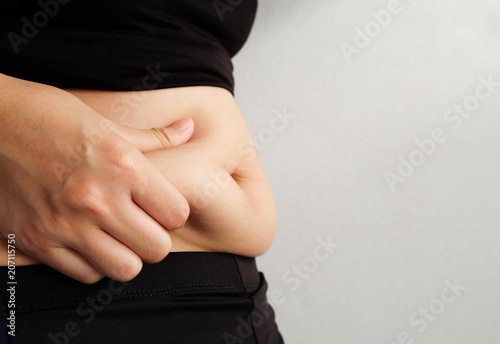Side of woman hand catching fat body belly paunch , diabetic risk factor .