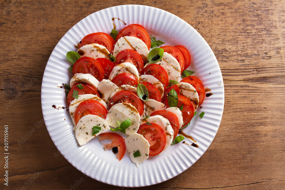 Italian caprese salad with sliced tomatoes, mozzarella cheese, basil, olive oil and balsamic vinegar. View from above, top studio shot Italian caprese salad with sliced tomatoes, mozzarella cheese, basil, olive oil and balsamic vinegar. View from above, top studio shot