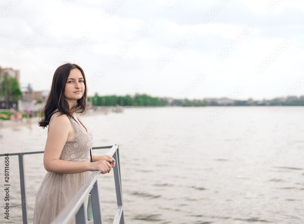 Young woman walks along waterfront. Brunette woman in gray summer dress