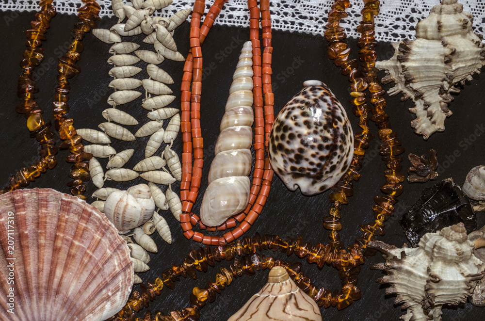 Naklejka premium A group of shells and stones with amber and coral beads on a white openwork border lie on black plywood 
