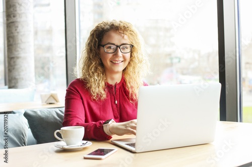 Beautiful young woman working remotely on her fashionable laptop at hipster coffee shop. Happy female freelancer with trendy wrist watch, cup of cappuccino and notebook computer, big window background Free Download Beautiful young woman working remotely on her fashionable laptop at hipster coffee shop. Happy female freelancer with trendy wrist watch, cup of cappuccino and notebook computer, big window background - GFXLoad