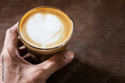 Hand holding cup of hot coffee with foam and smoke on table in the morning. copyspace for your text