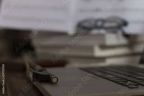 Detail of a fiddlestick resting on a laptop, in the background music sheets are visible.