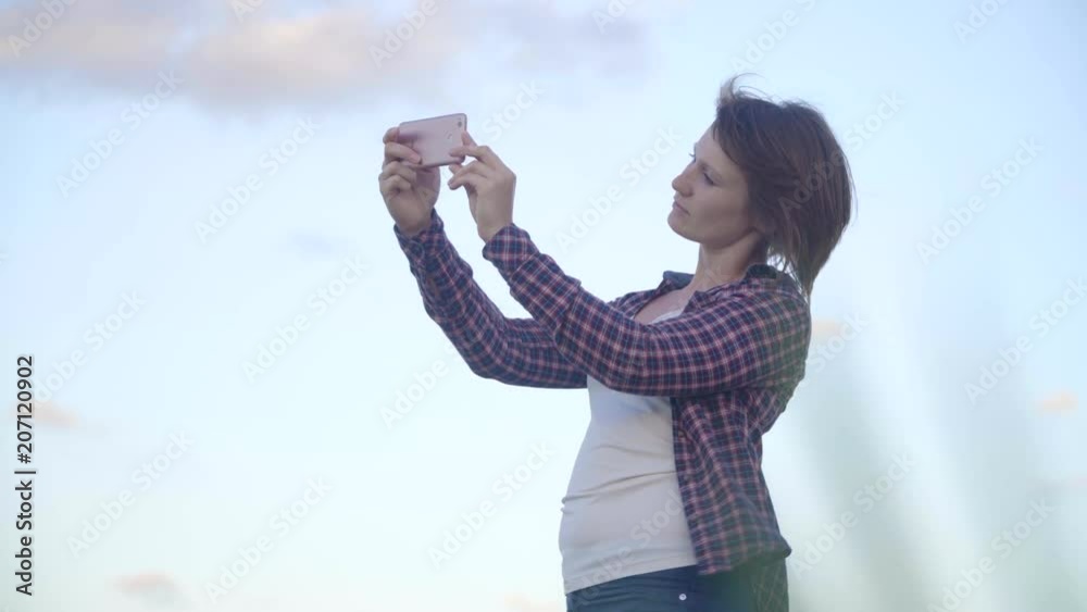 Young woman standing on top of a cliff on an island takes pictures on a smartphone.Sunset Young woman standing on top of a cliff on an island takes pictures on a smartphone.Sunset