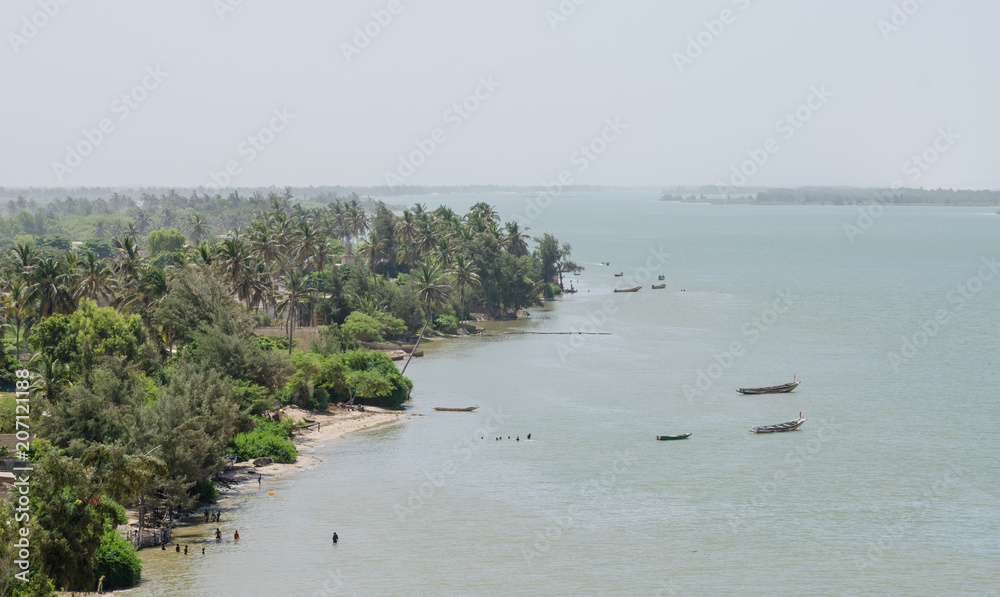 Tropical coast line with narrow gray beach, palms, lush vegetation and wooden fishing boats, Ndiebene, Senegal