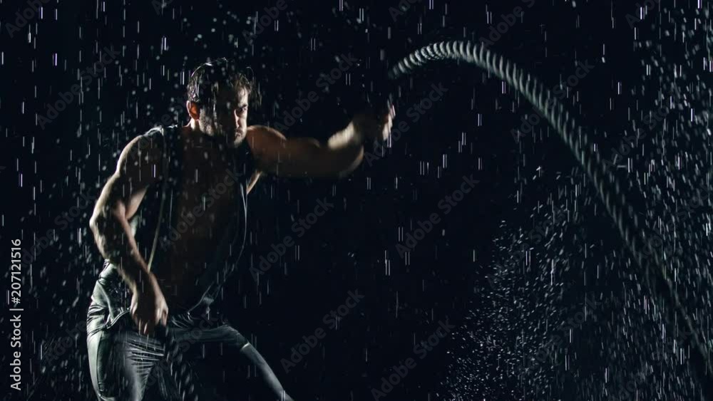 Athletic man working out with battle ropes in the rain. Slow Motion.
