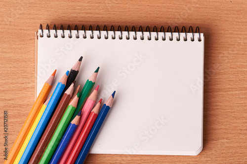 Open notebook on wooden background with colorful pencils. Flat lay