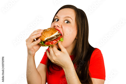 Young woman holds hamburger and eats him, isolated on white background. Looks in camera.