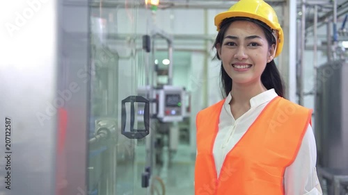 Woman industrial engineer at work in factory. Beautiful young chinese engineer working in large factory. With safety helmet and jacket. High tech automatic machine in background.