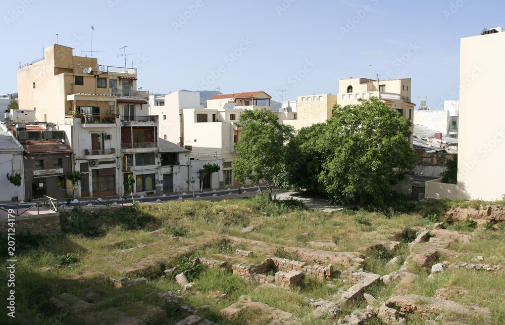 The ancient ruins near white houses and green trees in the small old town in Greece.