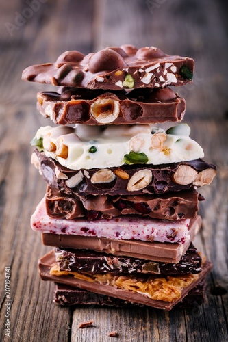 Stack of white, milk and dark chocolate with nuts, caramel and fruits and berries on wooden background.