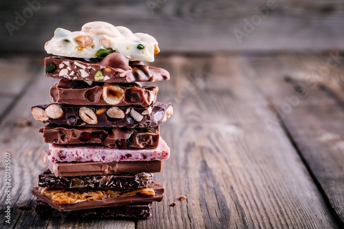 Stack of white, milk and dark chocolate with nuts, caramel and fruits and berries on wooden background.