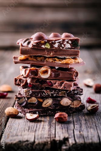 Stack of  milk and dark chocolate with nuts, caramel and fruits and berries on wooden background.