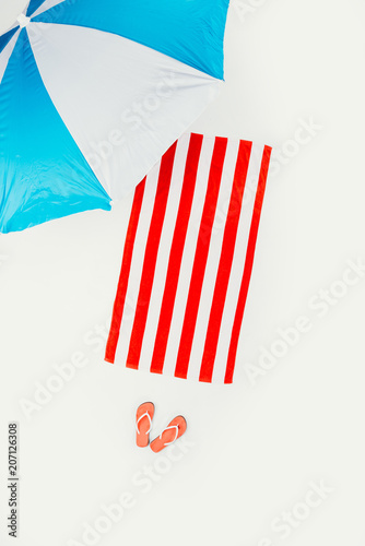 top view of beach umbrella, striped towel and flip flops isolated on white