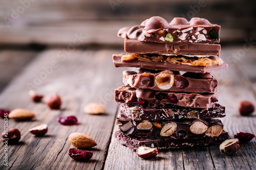Fototapete Stack of  milk and dark chocolate with nuts, caramel and fruits and berries on wooden background