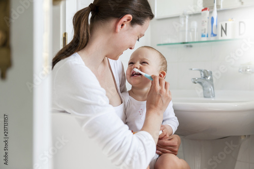Mother brushing baby's teeth in bathroom photo