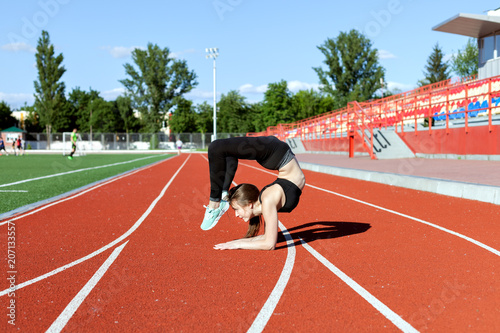 Young woman is engaged in fitness in the stadium. She makes a handstand.