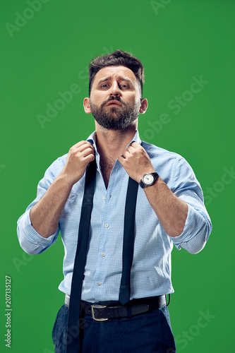 Male beauty concept. Portrait of a fashionable young man with stylish haircut wearing trendy suit posing over green background.