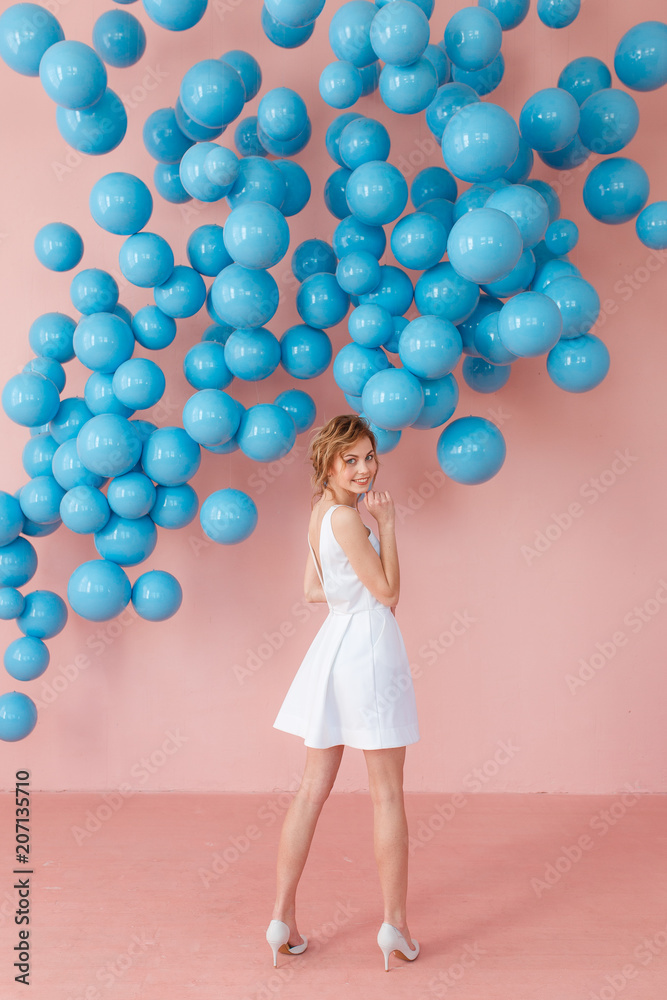 Fototapeta premium Back view of beautiful young woman standing over pink background and blue balls