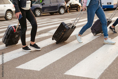 Cropped image of three women walking across pedestrian crossing, and carrying luggage after arrival to airport. Air travel or holiday concept