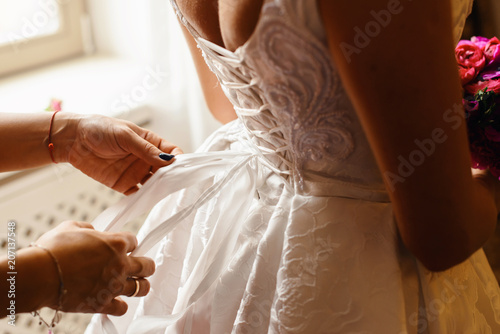 Bridesmaid makes bow knot on the back of brides wedding dress. Bridal morning of wedding day