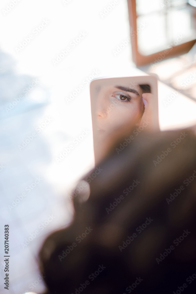 Feflection of woman eye in a small mirror. Woman doing make-up. Sunny day