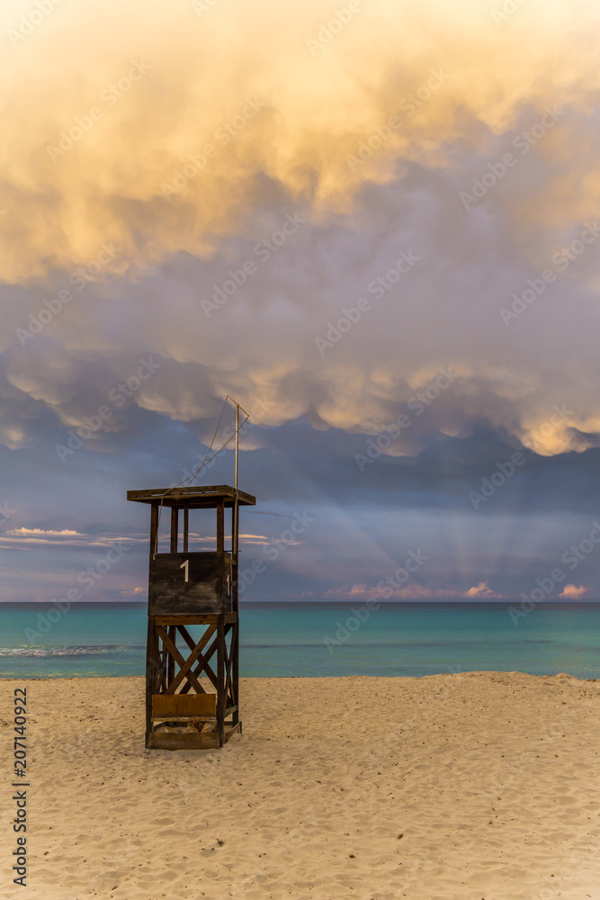 Mallorca, Golden light of dawning sun in impressive cloudscape natural spectacle at beach with lifeguard house
