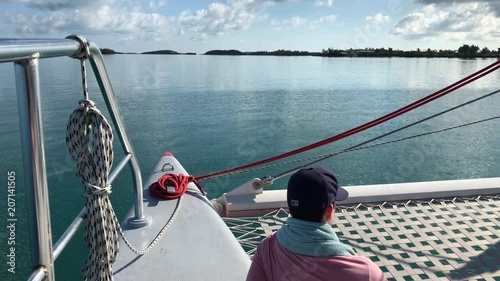 POV catamaran with man looking out over blue harbor, Bermuda