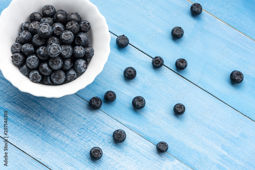 Fresh ripe blueberries in ceramic bowl on wooden table plank, top view