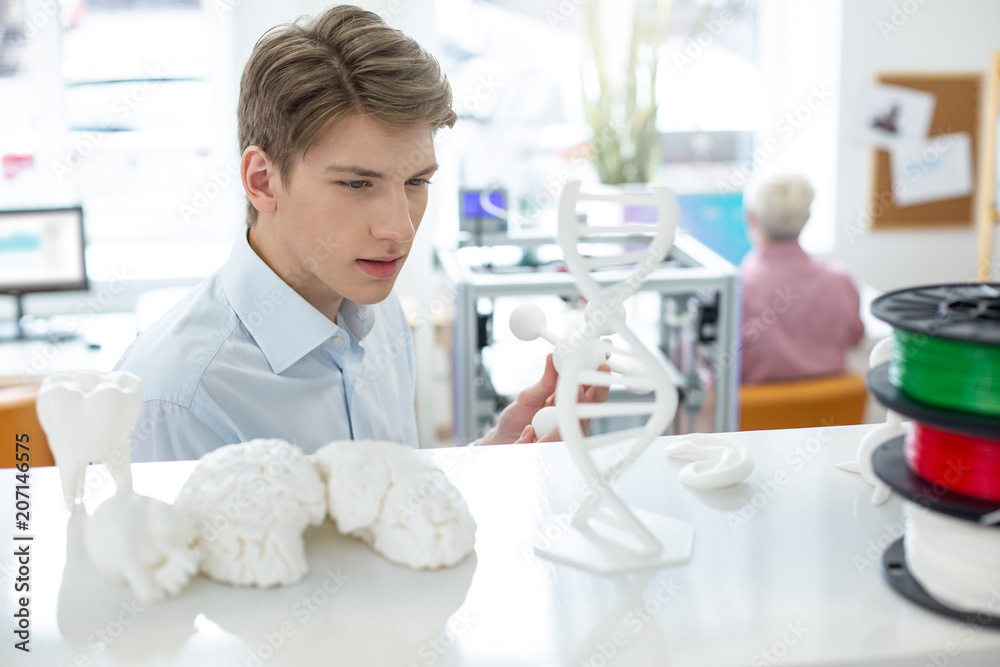 Obraz premium Admiring high quality. Charming young man examining a 3D atom model made with a 3D printer, having taken it from the shelf