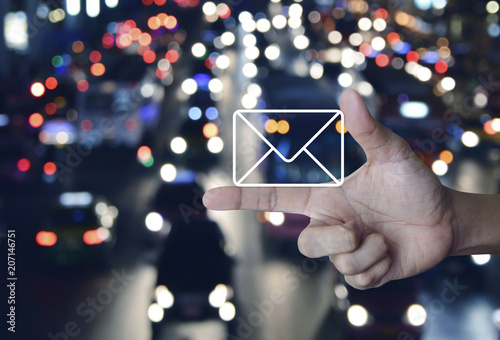 Mail icon on finger over blurred colourful night light city with cars, Contact us concept