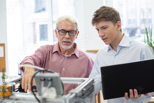 Nice teacher. White-haired senior engineer teaching his young student about 3D printers and telling him about the work algorithm