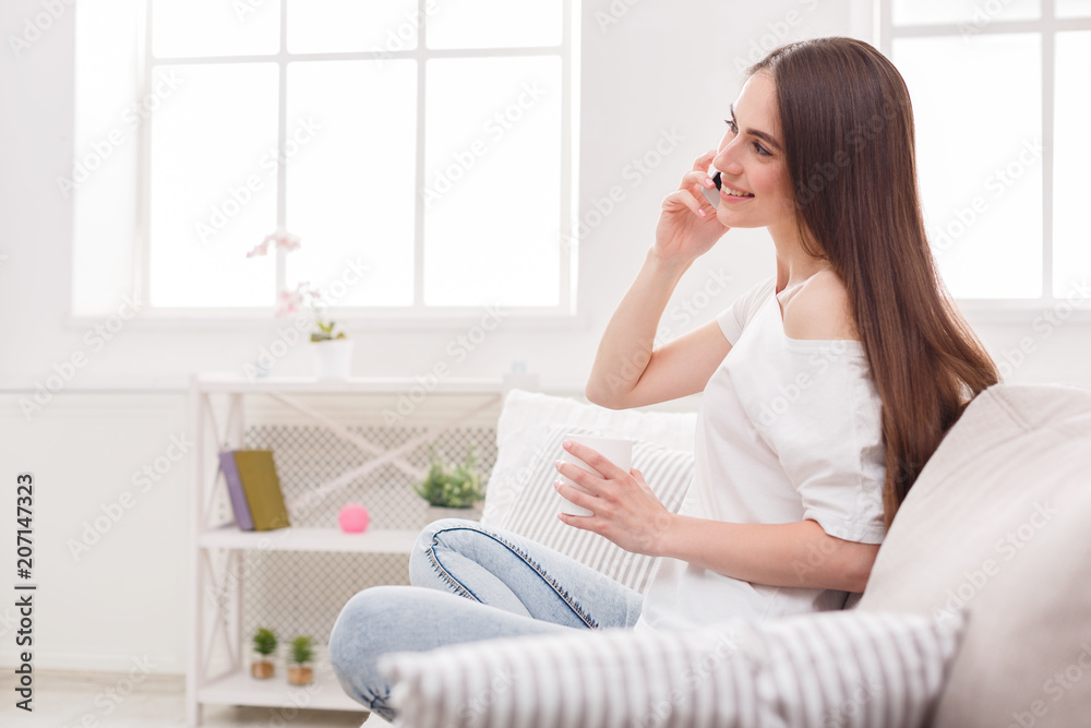 Young woman sitting on sofa with cell phone and coffee Young woman sitting on sofa with cell phone and coffee
