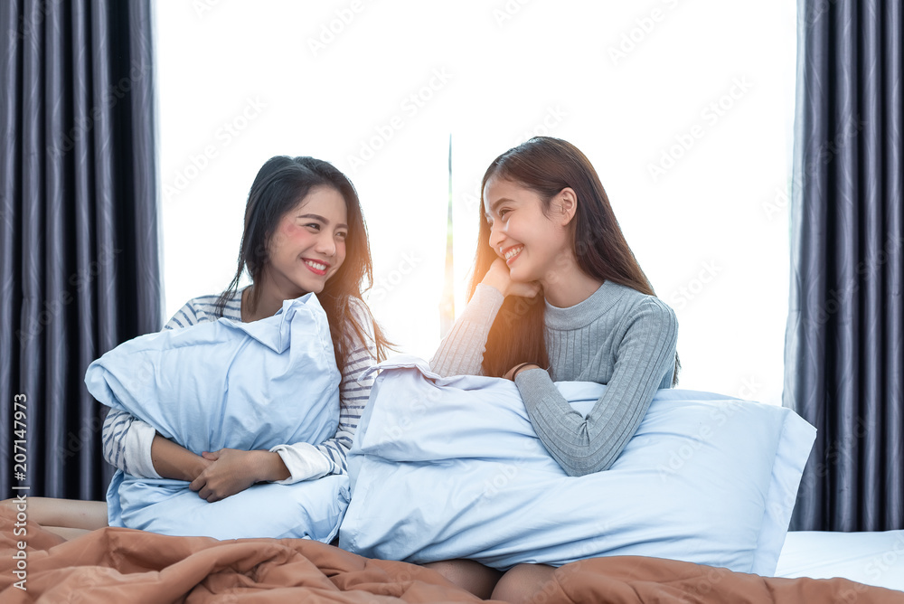 Two Asian Lesbian women looking together in bedroom. Couple people and Beauty concept. Happy lifestyles and home sweet home theme. Cushion pillow element and window background.