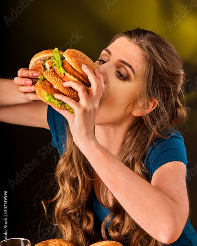 Woman eating hamburger. Student consume fast food on table. Girl trying to eat junk on dark background. Cook teaches cook and shares recipes. Expensive fast food restaurant.