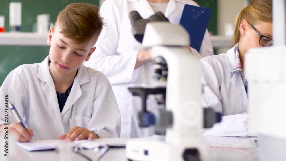 education, science and children concept - teacher and students studying chemistry at school laboratory and writing to workbooks education, science and children concept - teacher and students studying chemistry at school laboratory and writing to workbooks
