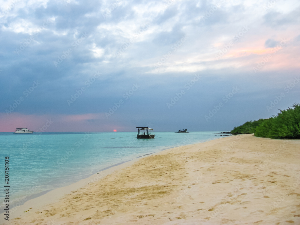 Maldives background. Sunset over the tropical sea and coral beach with colorful cloudy sky. Boats on the horizon. North Male Atoll Asdu, Indian Ocean. Maldives background. Sunset over the tropical sea and coral beach with colorful cloudy sky. Boats on the horizon. North Male Atoll Asdu, Indian Ocean.