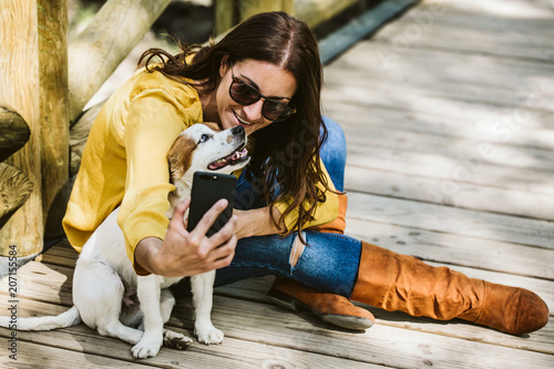 Young beautiful woman taking photograph of her sweet dog playfuly in a lovely park of the center of Madrid. Seated in a wooden floor. Lifestyle