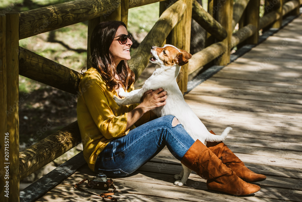 Young beautiful woman playing with her sweet little dog in a lovely park of the center of Madrid. Seated in a wooden floor. Lifestyle. Friendship. Young beautiful woman playing with her sweet little dog in a lovely park of the center of Madrid. Seated in a wooden floor. Lifestyle. Friendship.