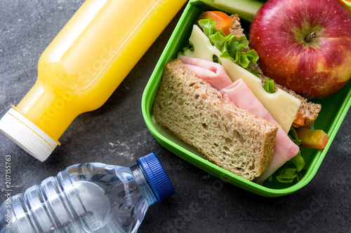 Healthy school lunch box: Sandwich, vegetables ,fruit and juice on black stone. Top view photo