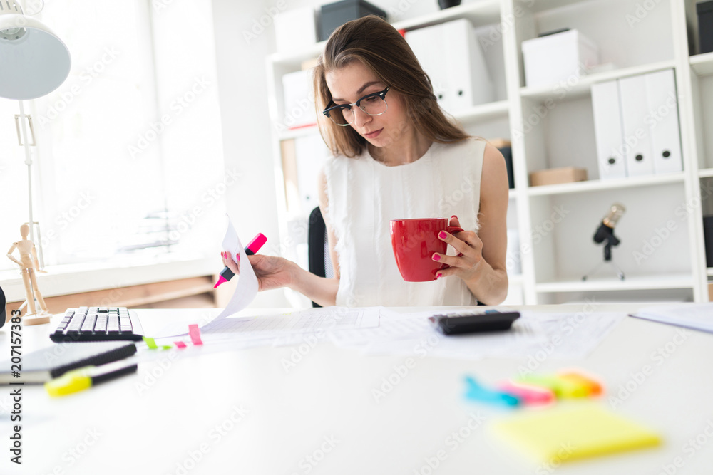 A young girl in the office holds a pink marker, a red mug and works with documents. A young girl in the office holds a pink marker, a red mug and works with documents.