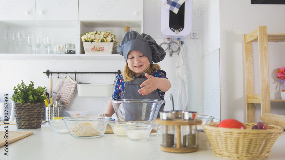 Cheerful little girl in apron rolls out the dough in the kitchen Cheerful little girl in apron rolls out the dough in the kitchen