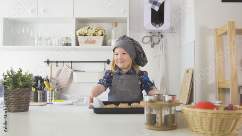 Preschool girl baker holding a baking sheet with cookies