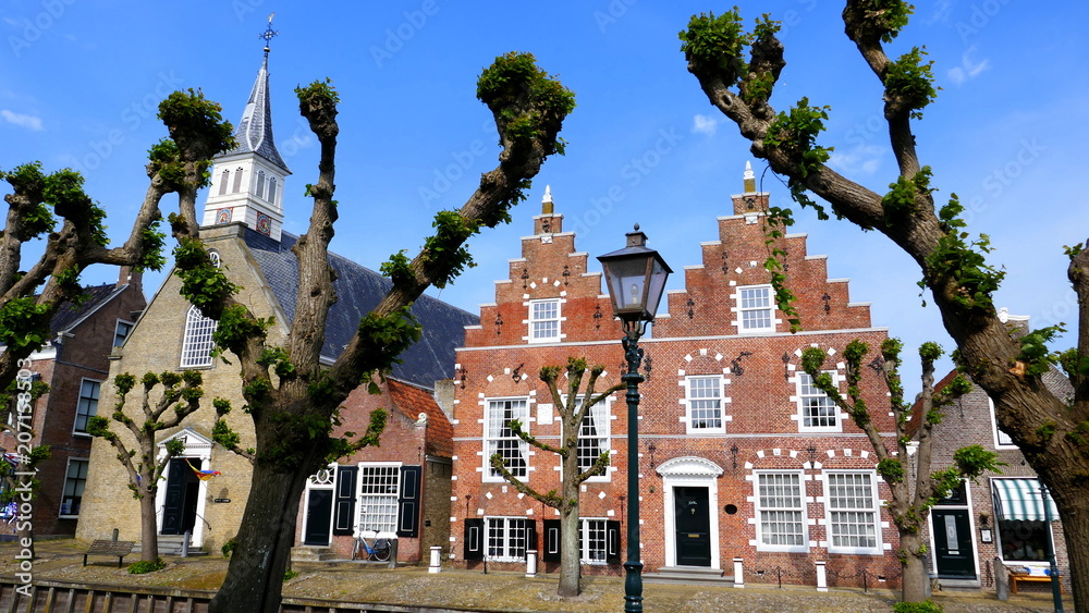 Fototapeta premium alte Häuser und Kirche in Sloten malerisch umrahmt von frisch aussprießenden Bäumen