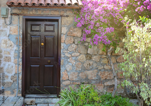 Brown wooden door in a stone wall under blooming bougainvillea