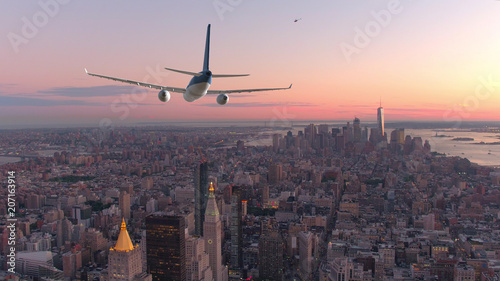 AERIAL: Passenger airplane flying over downtown Manhattan at beautiful sunset.