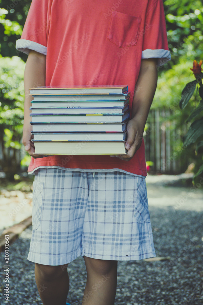 little boy is holding stack of books in the garden.